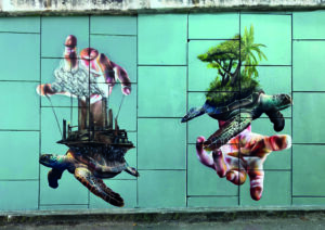 Street mural depicting turtles holding two different types of world, one guided by a hand (green) and one controlled by a hand above (black and dead).