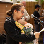 Woman holding a tiny baby to her chest while reading into a microphone