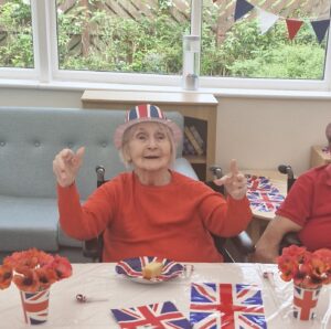 Care home resident wears a Union Jack hat with Union Jack flats and plate in front of her.